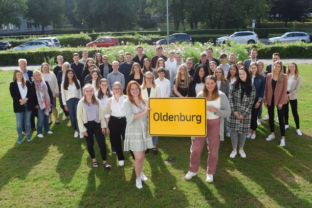 Auszubildende stehen mit Oldenburg-Schild auf einer Wiese. © Stadt Oldenburg