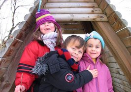 Drei Kinder stehen vor einer Holzhütte. Foto: adel/pixelio.de
